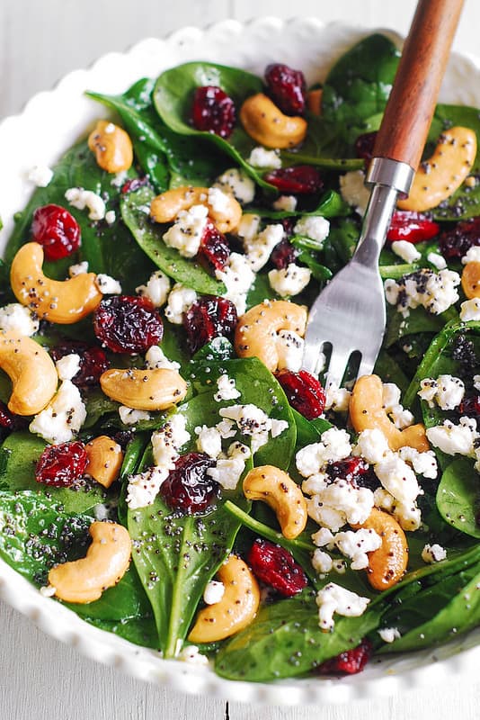Cranberry Spinach Salad with Cashews and Goat Cheese in a white bowl