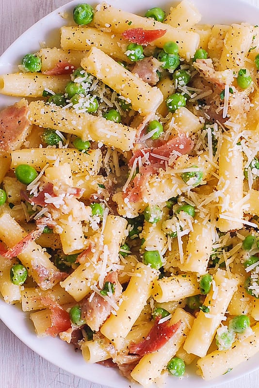 Pasta with prosciutto and peas on a white plate