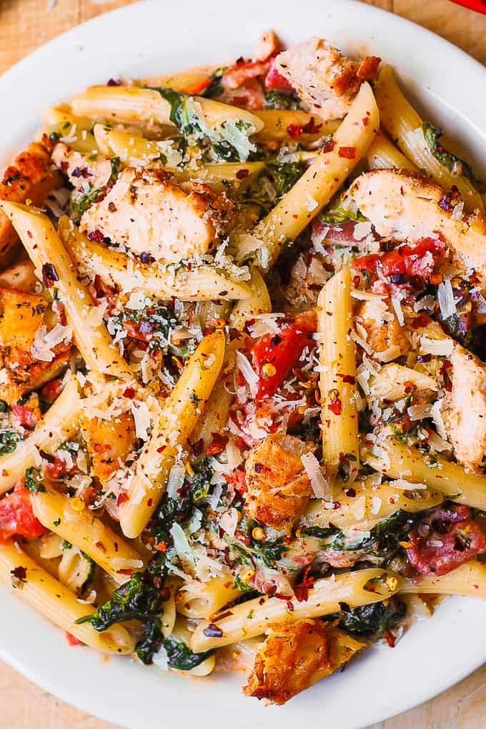 chicken bacon pasta with spinach tomatoes on a white plate
