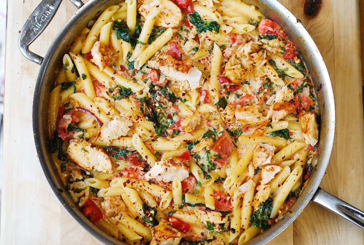 Chicken and Bacon Pasta with Spinach and Tomatoes in Garlic Cream Sauce in a stainless steel pan.