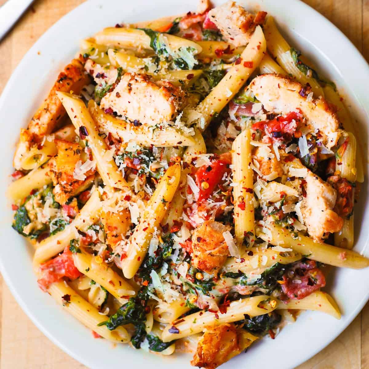 Creamy Chicken and Bacon Pasta with Spinach and Tomatoes - on a white plate.