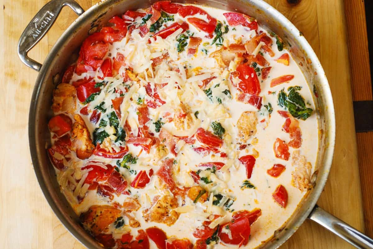 creamy sauce with veggies and chicken and bacon in a stainless steel pan.