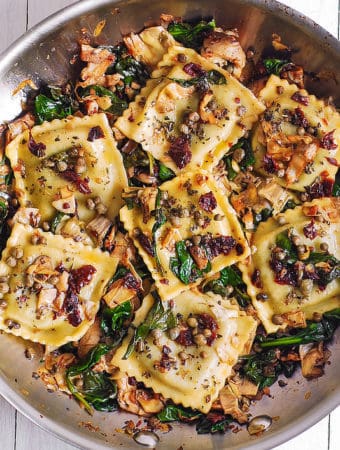 Italian Ravioli with Spinach, Sun-Dried Tomatoes, Artichokes, Capers in a stainless steel skillet