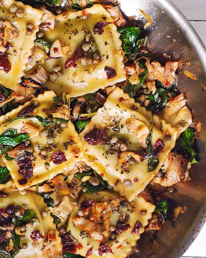 italian ravioli with sun-dried tomatoes, spinach, and artichokes - in a stainless steel skillet.