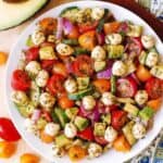 A bowl of salad with cherry tomatoes, mozzarella balls, red onion, cucumber, and avocado, all tossed in a green herb dressing.