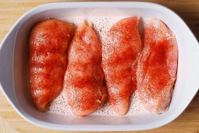 4 raw chicken breasts topped with chili powder in a white casserole dish