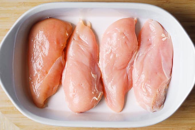 4 raw chicken breasts in a white casserole dish