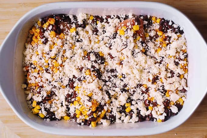 4 raw chicken breasts topped with chili powder, corn kernels, black beans, Cotija cheese in a white casserole dish