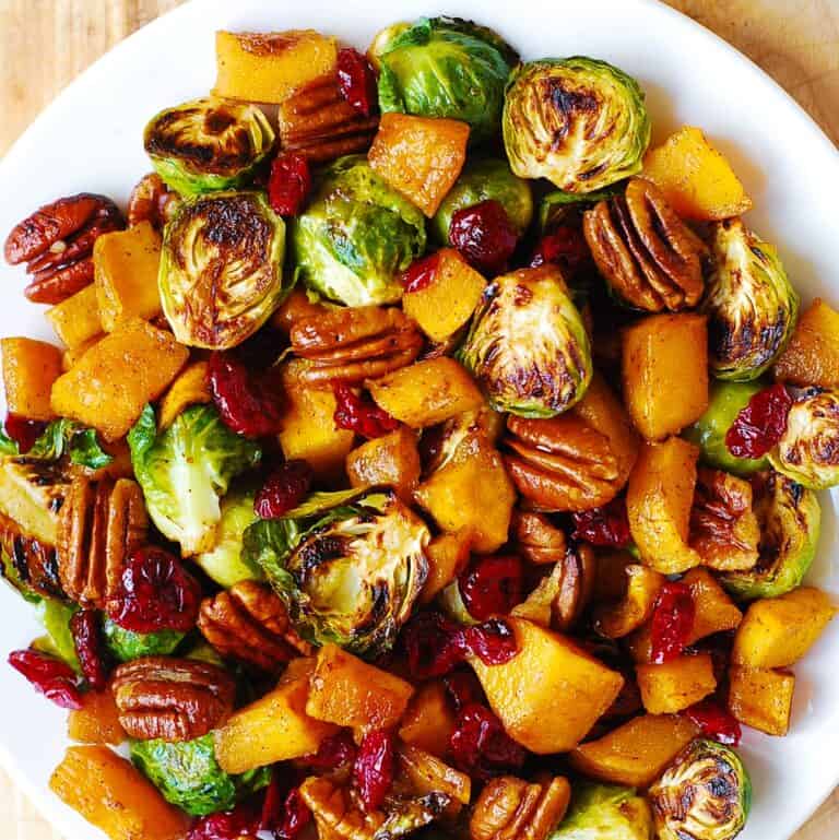 A white plate filled with roasted Brussels sprouts, chunks of roasted butternut squash, pecans, and dried cranberries, all mixed together for a colorful and hearty dish.