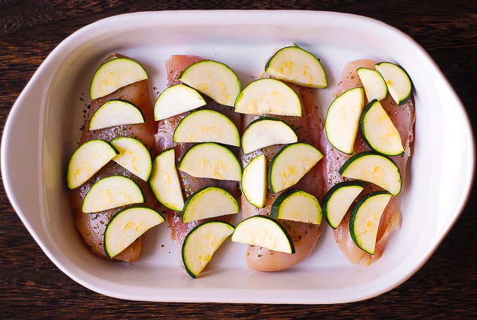chicken breasts topped with sliced zucchini in a casserole dish