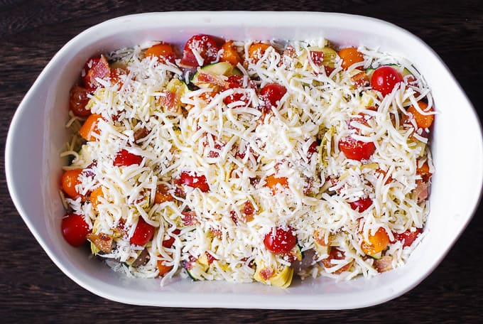 chicken, tomatoes, artichokes, zucchini, topped with Mozzarella cheese in a white casserole dish