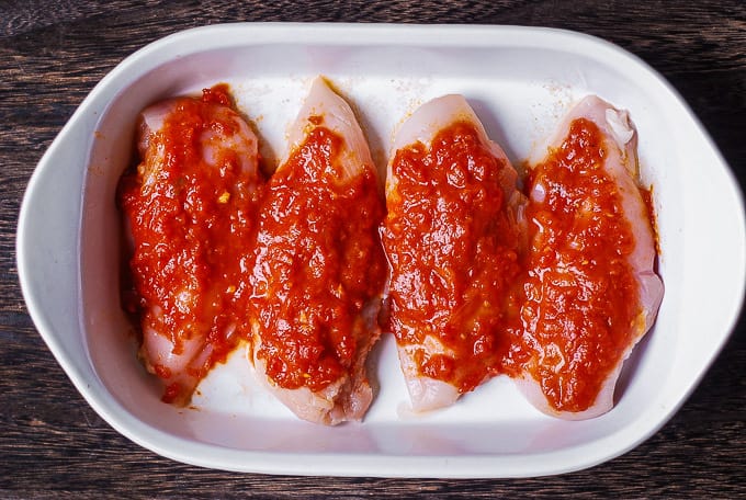 marinara sauce on top of chicken breasts in a casserole dish