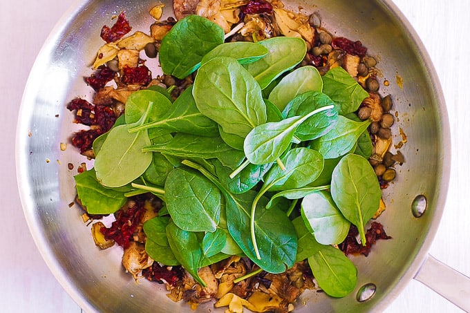 add spinach to artichokes, sun-dried tomatoes, capers, garlic in a skillet