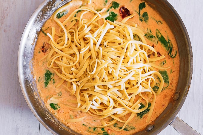 adding linguine to the skillet with sun-dried tomato sauce and spinach