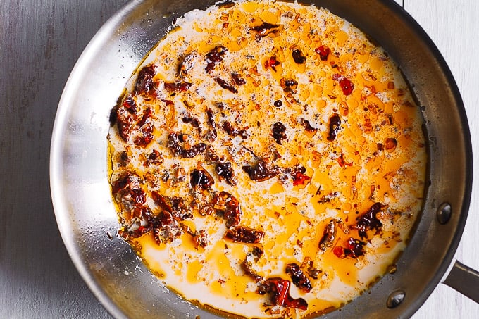 adding half-and-half to sun-dried tomatoes and garlic and olive oil in a skillet