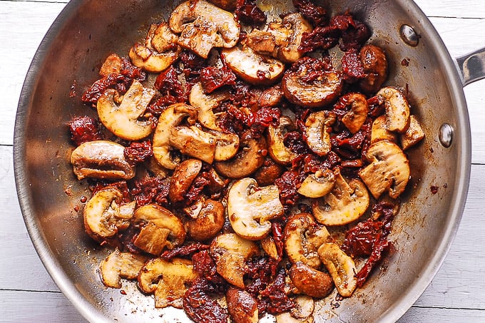 cooked mushrooms with sun-dried tomatoes in a skillet