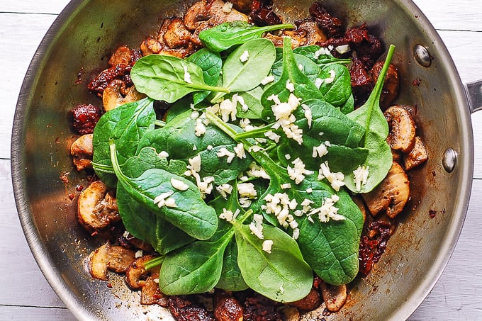 cooked mushrooms, sun-dried tomatoes, spinach, minced garlic in a skillet