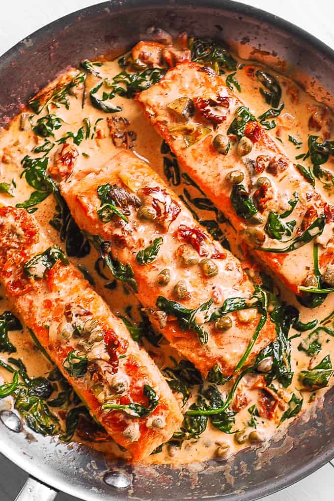 3 creamy tuscan salmon fillets with spinach, artichokes, sun-dried tomatoes, capers in a stainless steel skillet