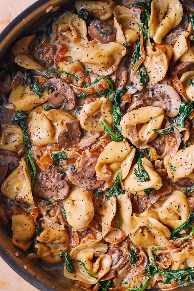 creamy spinach mushroom tortellini with caramelized onions in a stainless steel skillet