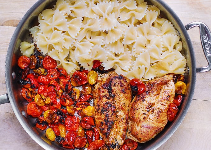 cooked chicken breasts, roasted tomatoes, and cooked bow-tie pasta in a large skillet