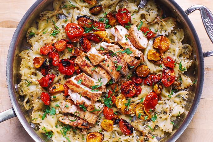 sliced cooked chicken, roasted tomatoes on top of bow tie pasta in a large skillet