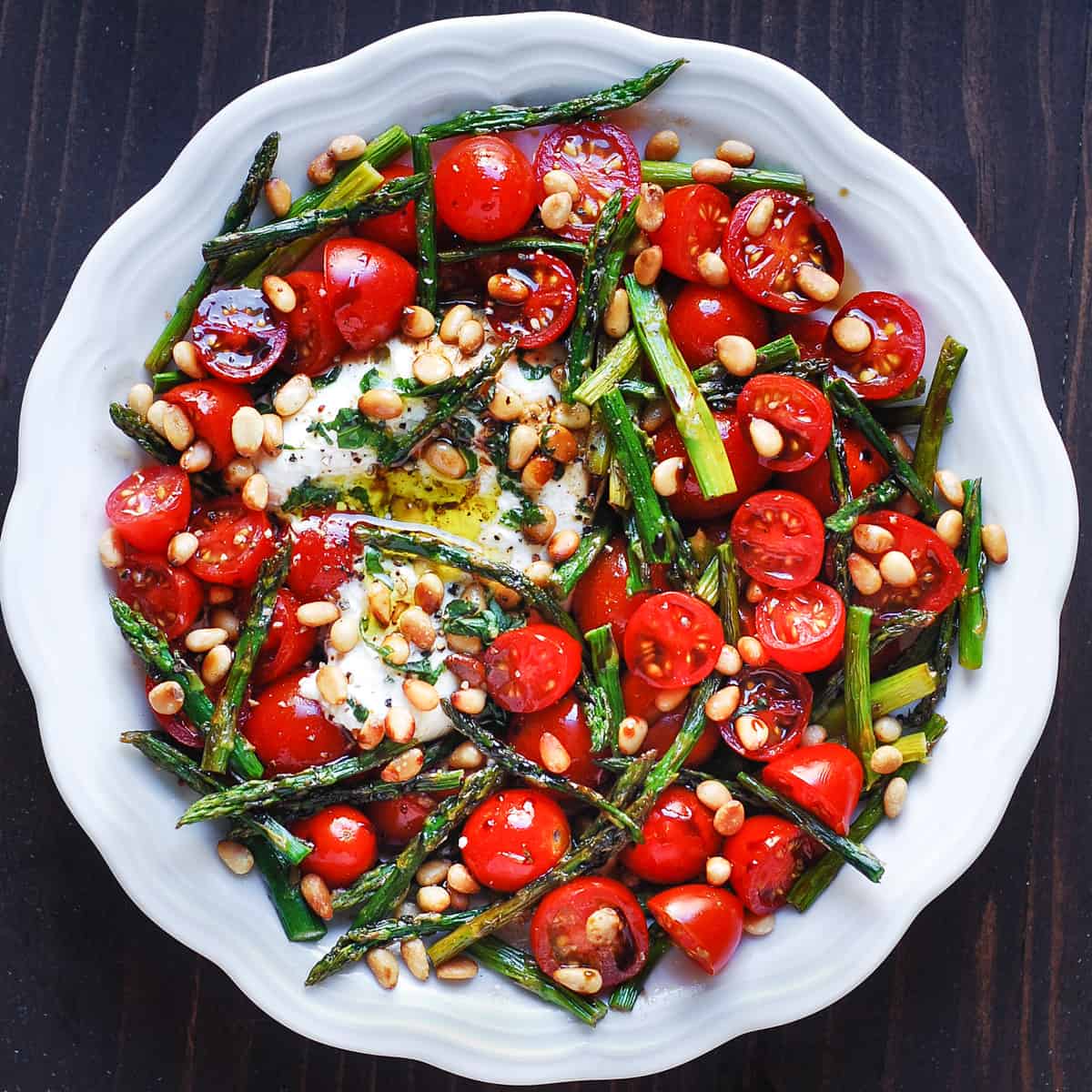 asparagus tomato salad with burrata cheese and pine nuts in a white bowl