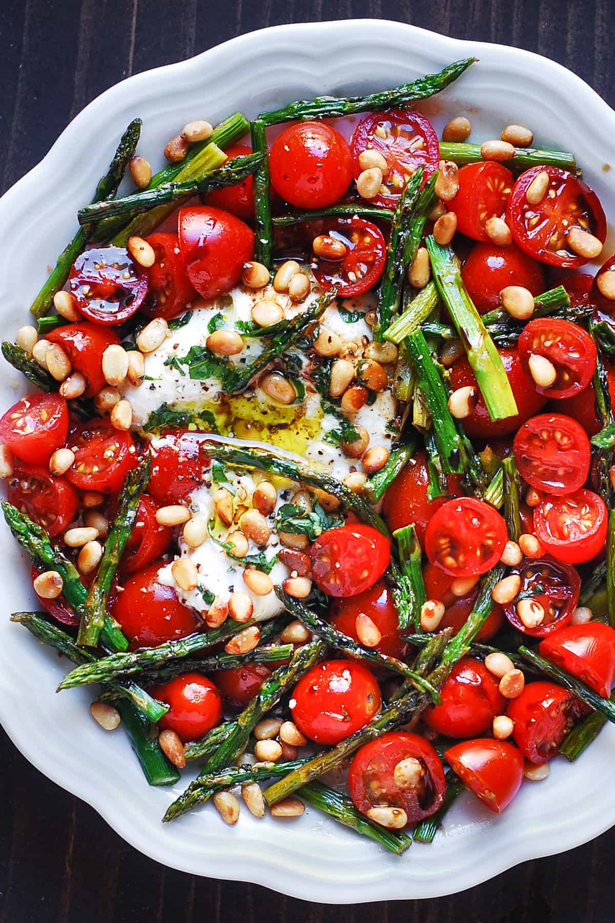 asparagus tomato salad with burrata cheese and pine nuts in a white bowl
