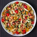 chicken bacon zucchini pasta with tomatoes and pine nuts on a white plate