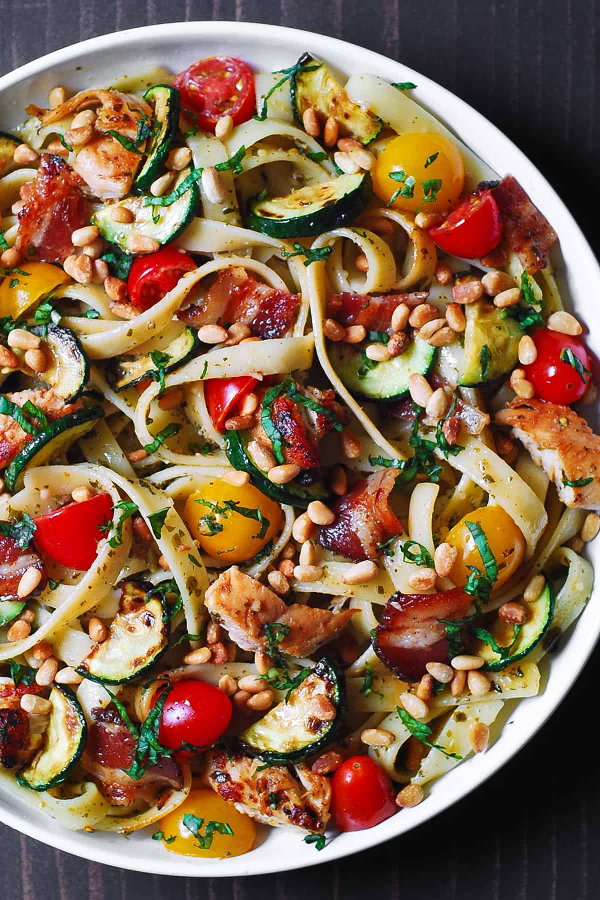 chicken bacon zucchini pasta with cherry tomatoes and pine nuts on a white pasta plate