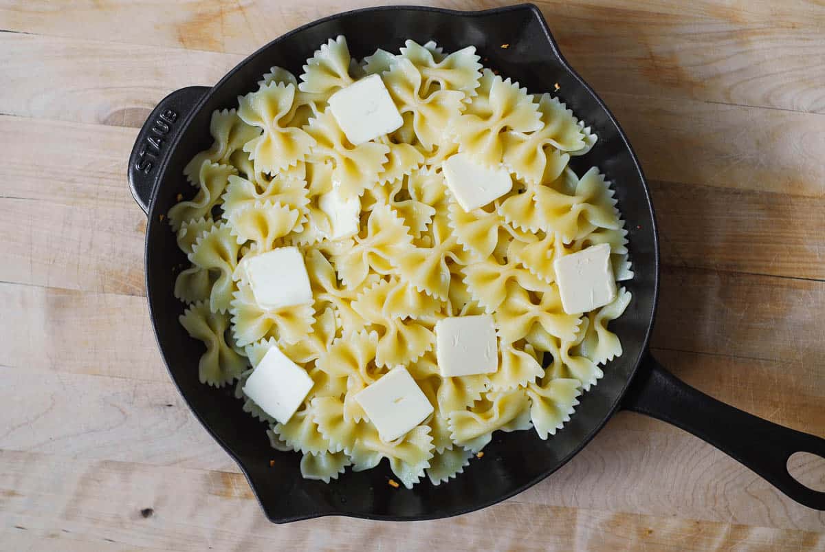 sliced butter on top of bow tie pasta in a cast iron skillet