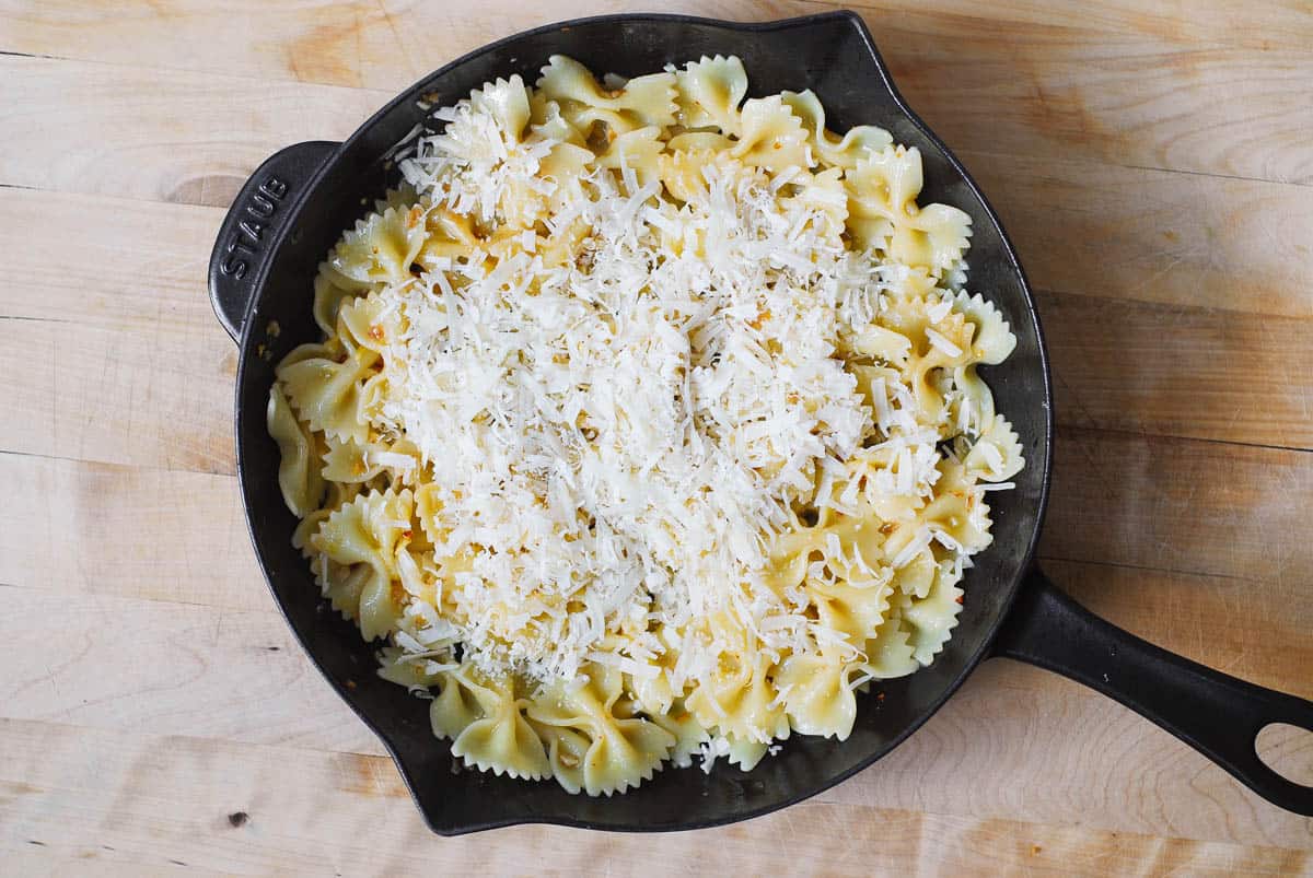 grated Parmesan cheese on top of bow tie pasta in a cast iron skillet