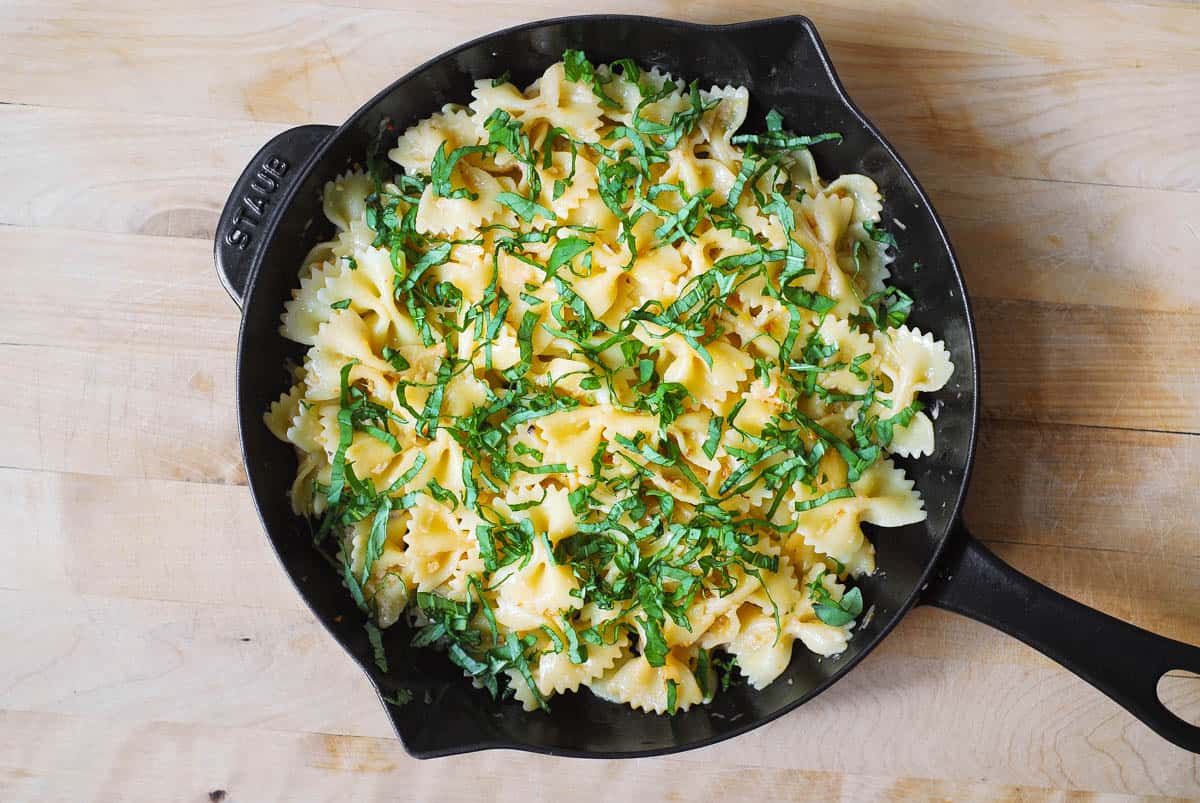 chopped fresh basil on top of bow tie pasta in a cast iron skillet