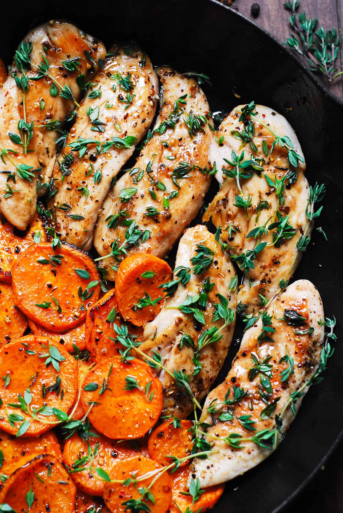 close-up of maple chicken with sweet potatoes and thyme in a cast-iron skillet