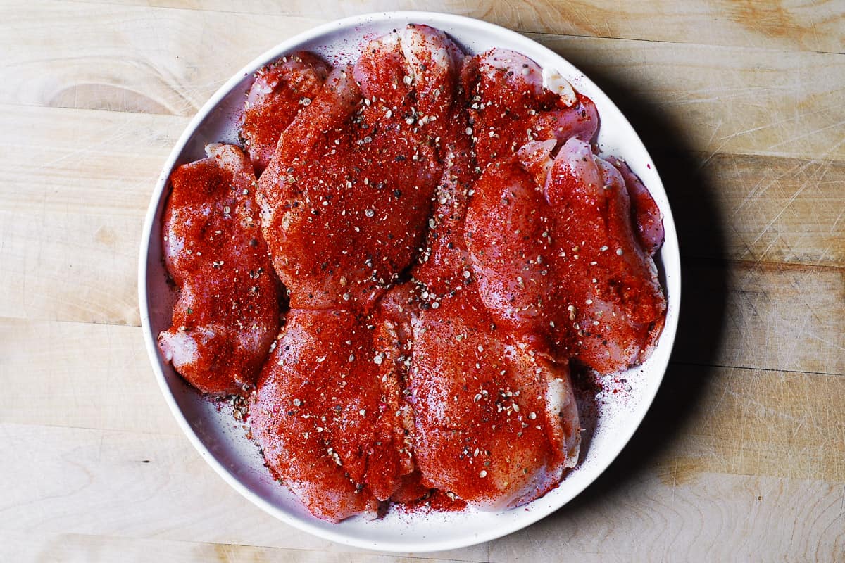 chicken thighs seasoned with salt, pepper, and smoked paprika on a white plate