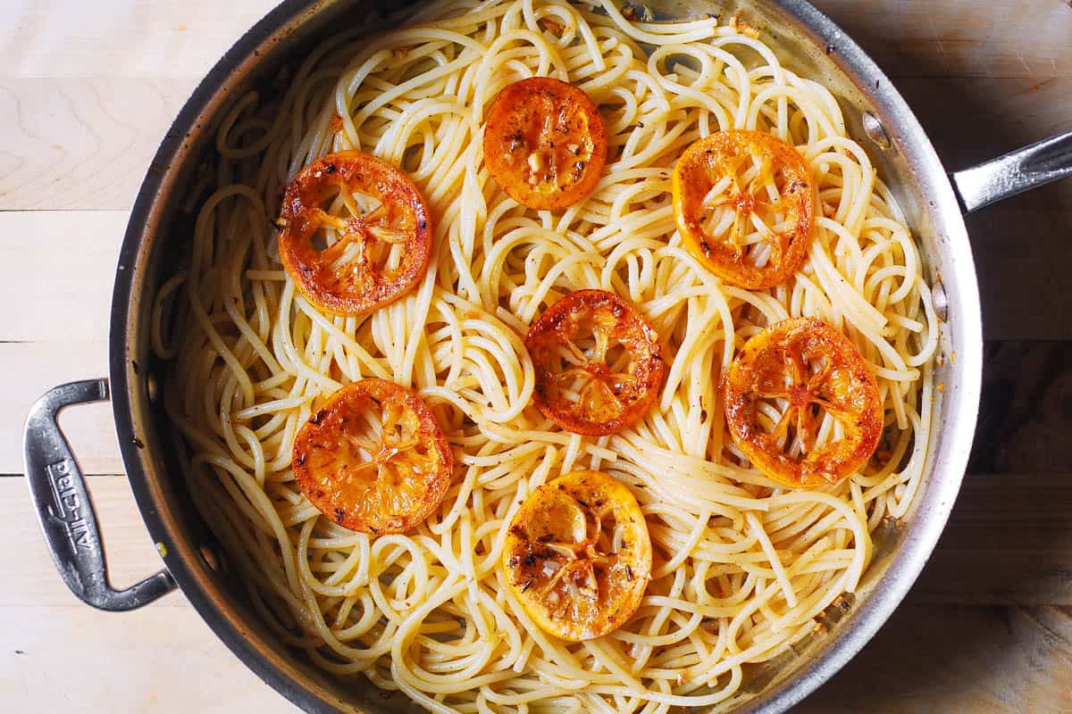 cooked spaghetti with lemon slices in a stainless steel pan
