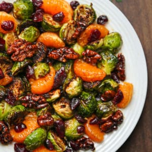 mandarin orange salad with dried cranberries, walnuts, roasted Brussels sprouts, and balsamic glaze on a white plate