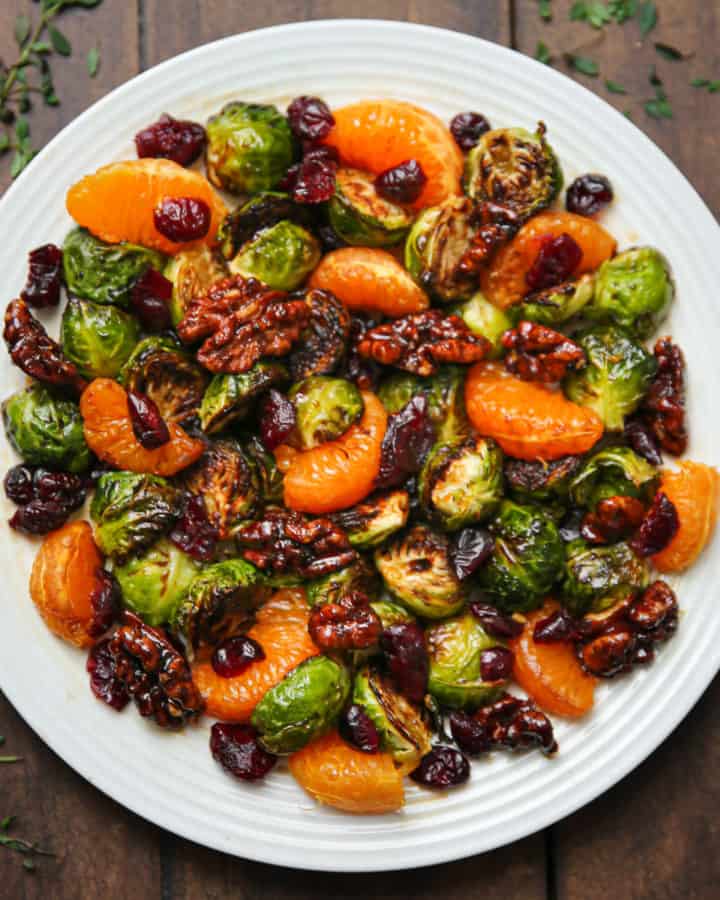 mandarin orange salad with dried cranberries, walnuts, roasted Brussels sprouts, and balsamic glaze on a white plate