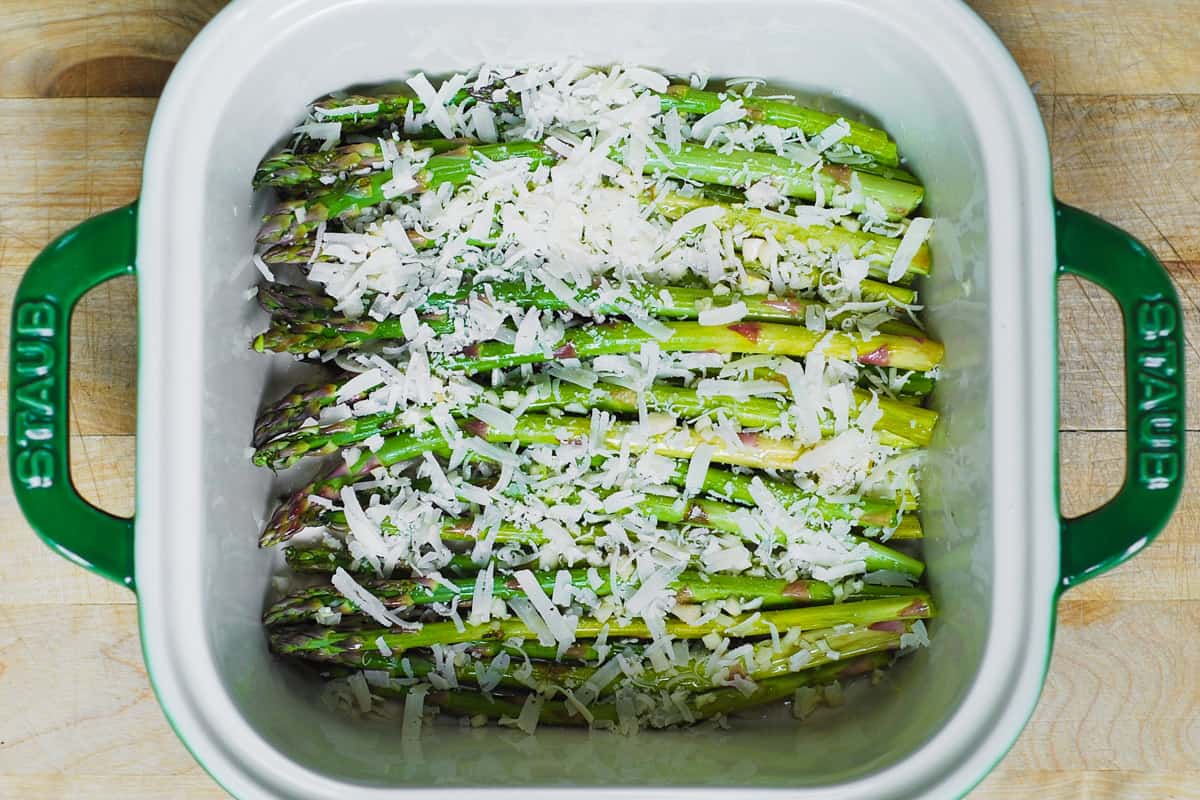 shredded parmesan on top of asparagus in a baking dish