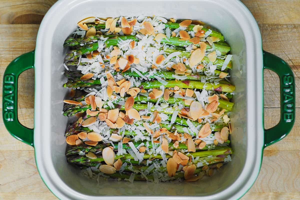 toasted almonds and shredded parmesan on top of asparagus in a baking dish
