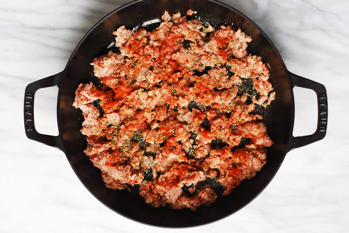 raw crumbled Italian sausage with seasonings in a cast-iron pan