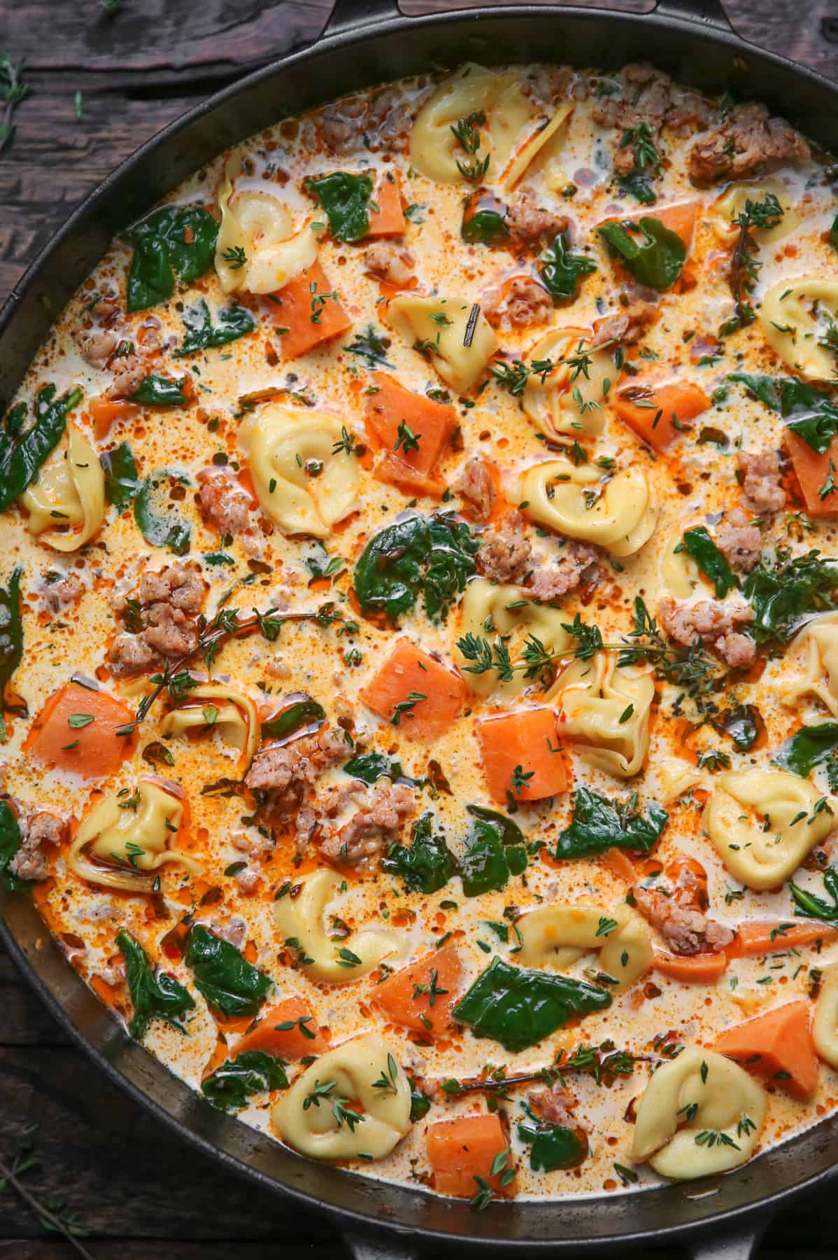 sausage tortellini soup with sweet potatoes and spinach in a cast iron pan