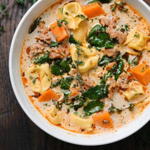 creamy sausage tortellini soup with sweet potatoes and spinach in a white bowl