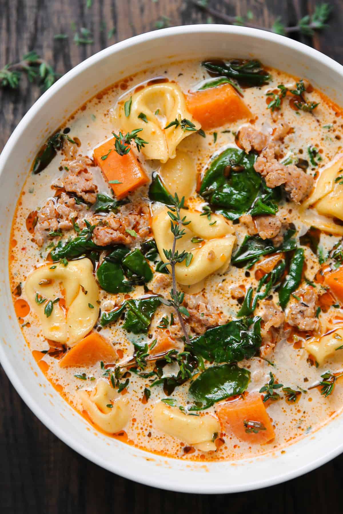 sausage tortellini soup with sweet potatoes and spinach in a white bowl