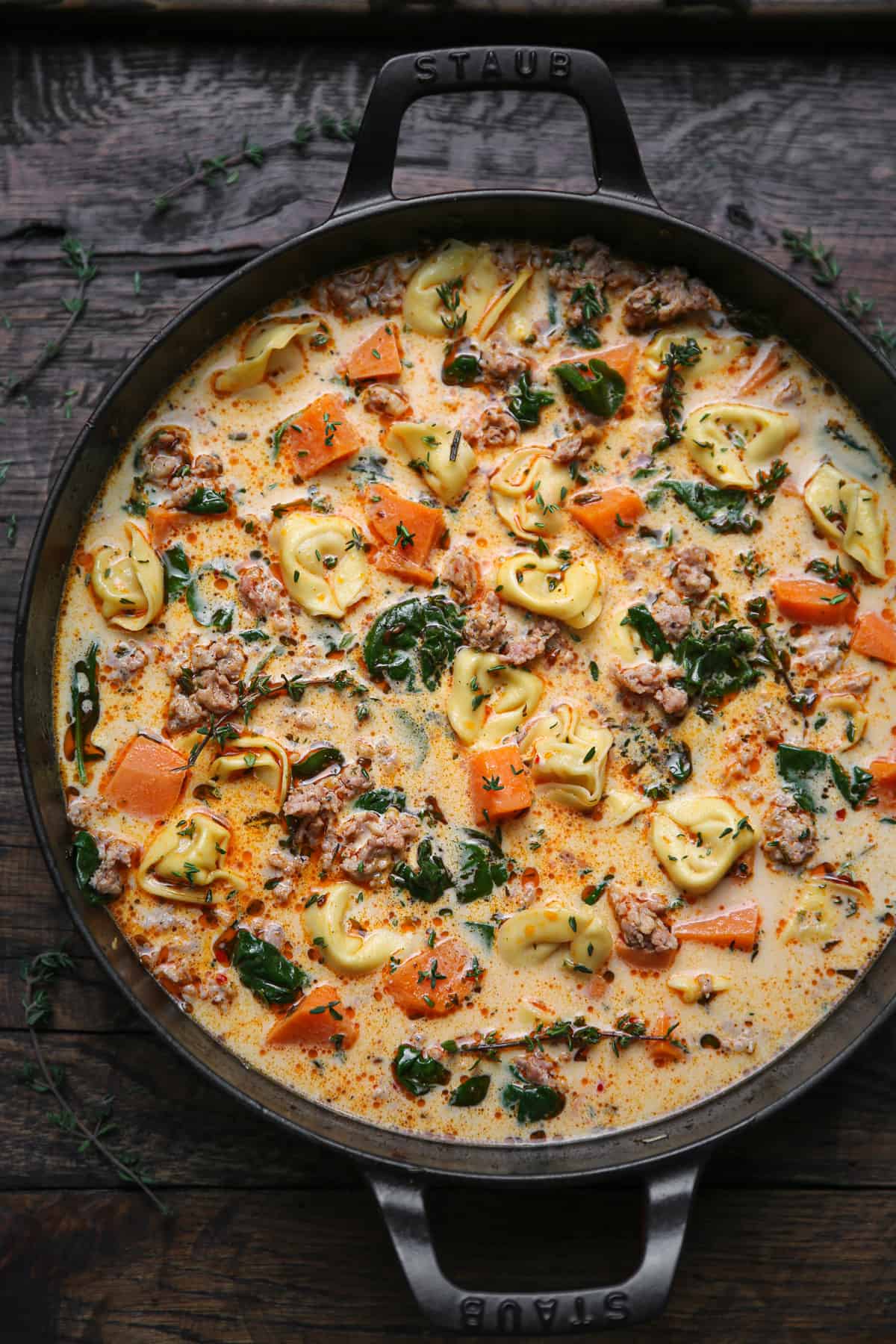 sausage tortellini soup with sweet potatoes and spinach in a cast iron pan