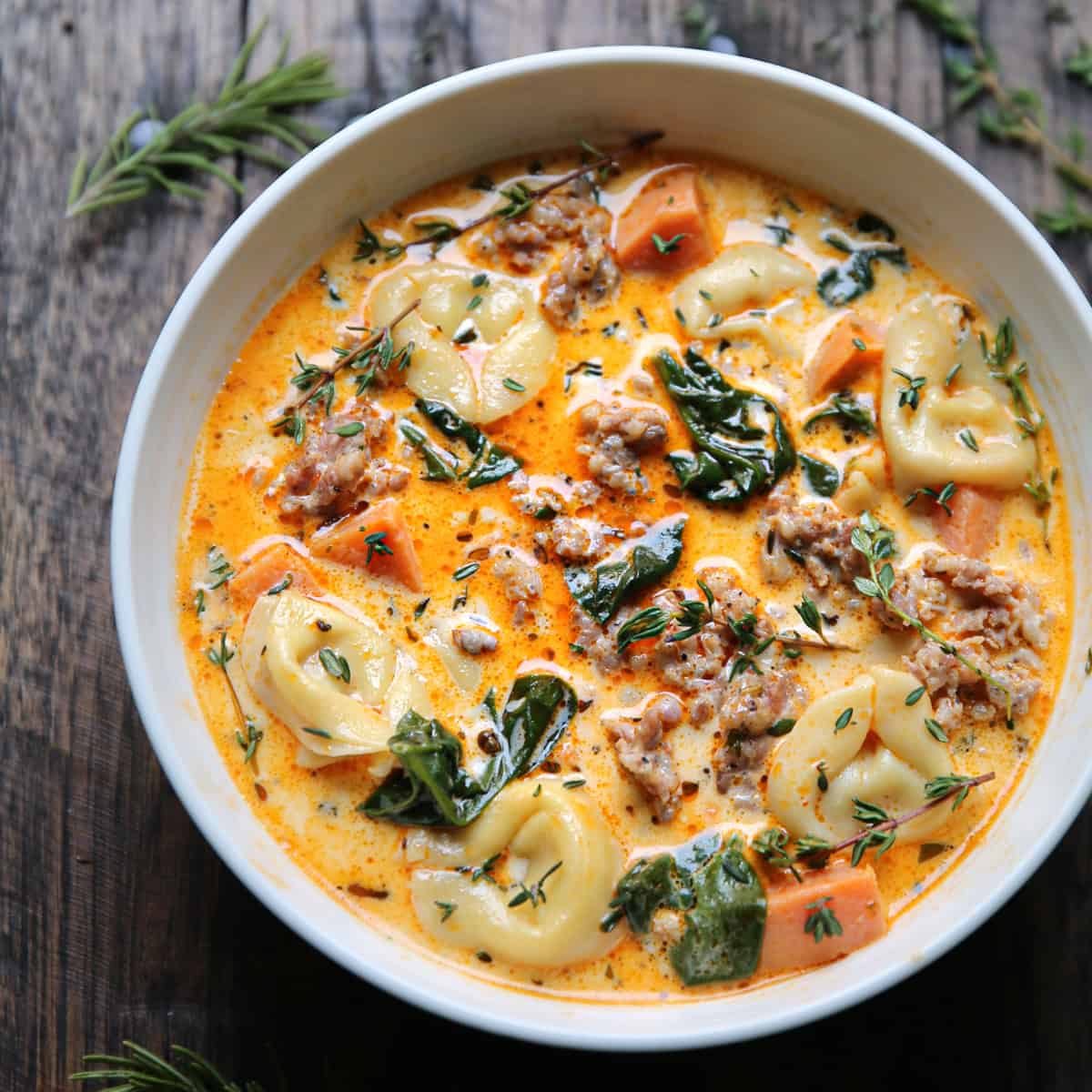 sausage tortellini soup with spinach and sweet potatoes - in a white bowl.