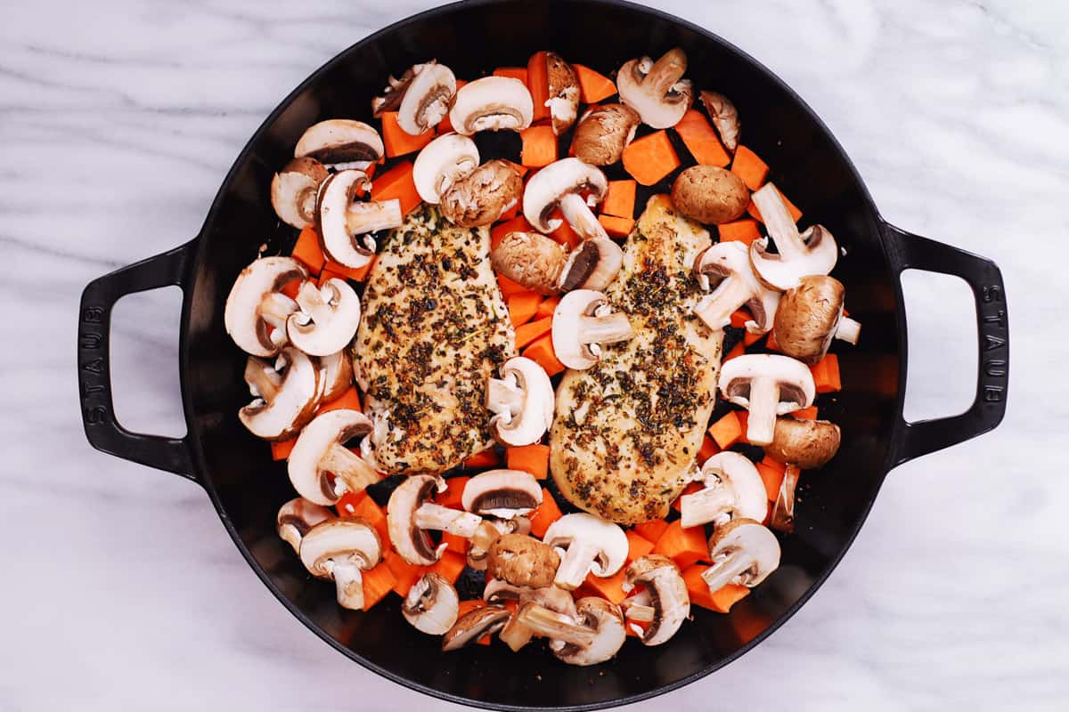 sliced mushrooms, sweet potatoes, and seared chicken in a cast iron pan