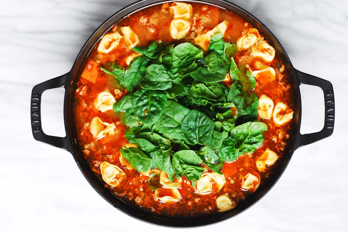 spinach and tortellini in the soup in a cast iron pan