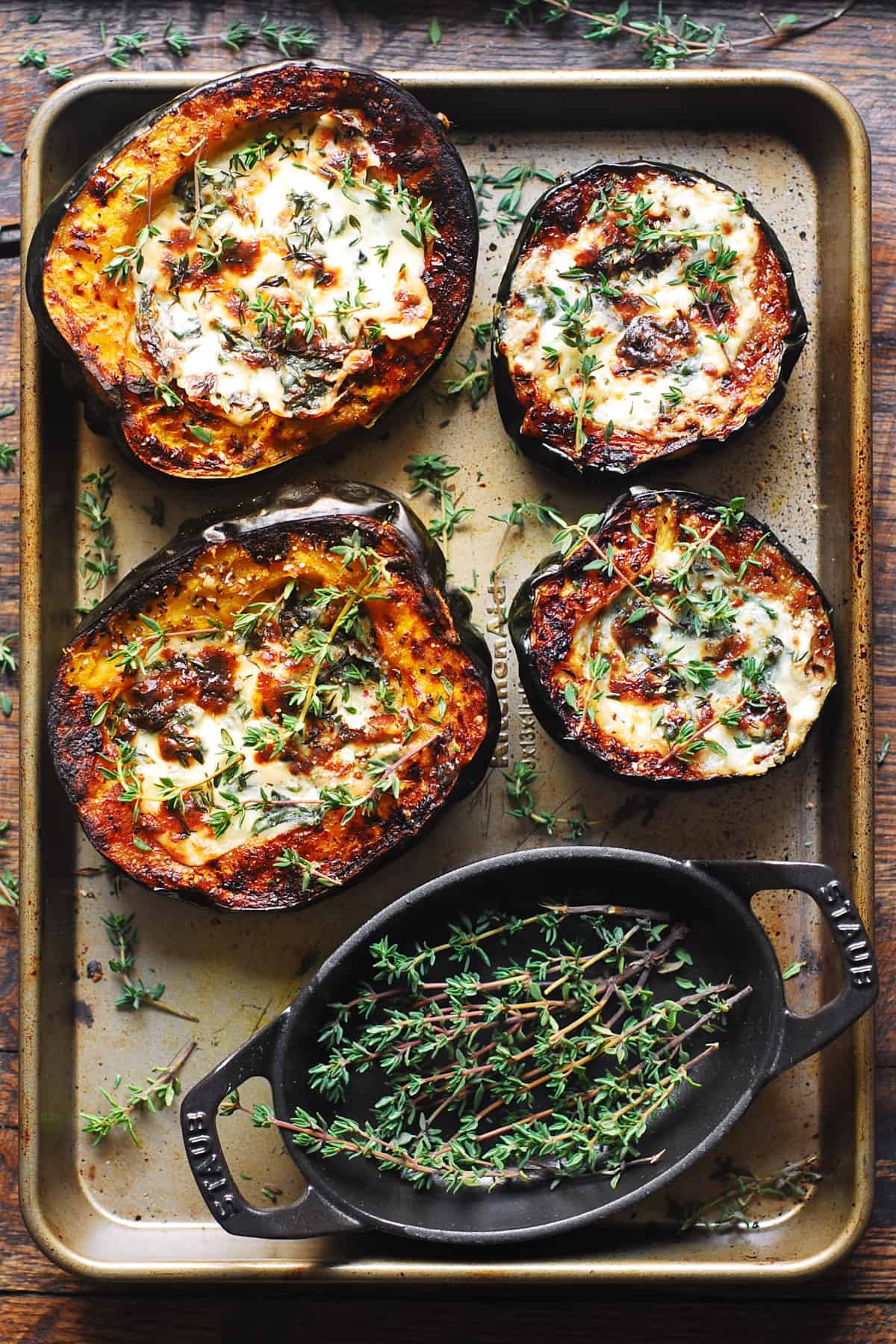 stuffed acorn squash with spinach and cheese on a baking sheet together with a small container of fresh thyme