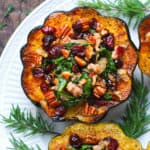 close-up of stuffed acorn squash with sausage, spinach, dried cranberries, and pecans on a white plate