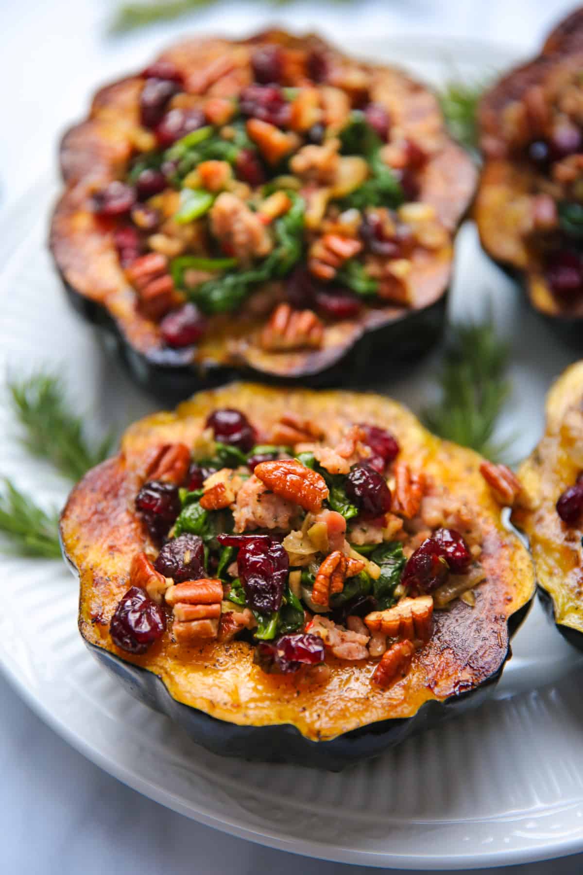 stuffed acorn squash with sausage, spinach, dried cranberries, and pecans on a white plate